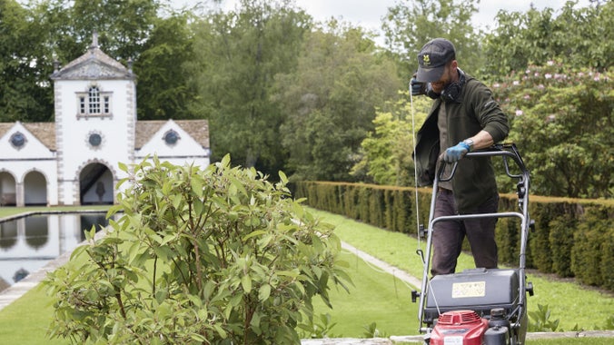 A gardener at Bodnant mowing the lawn in front of the Pin Mill